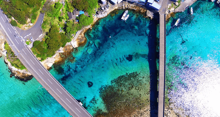 柏島を上空から撮影した写真。海の透明度の高さから、港や周辺の海域の「船が宙に浮いて見える」と、SNSで多くの話題を集めている観光スポット。実際に訪れると、橋の上からでも「肉眼で」水面の底や、泳いでいる魚を見つけることができるから驚きます・・・!
