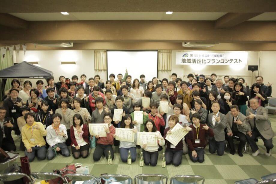 住吉氏が思い出の品として持ってきてくれたのは、こちらの一枚の写真。住吉氏が全国の大学生を静岡に集めて「地域活性化プランコンテスト」を行ったときの最後の集合写真。ここには、参加者である県外の大学生はもちろん、県内の大学生、コンテストを見にきてくれた地域の皆さん、イベントに協賛をしてくれた地元企業の方々、メンターとしてコンテストに関わってくれた都内大手企業の社員の方々、審査員が写っているそう。「コンテストをきっかけに “3つのしみん” が写っているこの写真が好きなんです」（住吉氏）